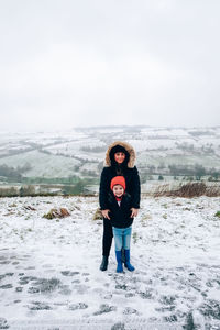 Portrait of cute boy with mother standing on snow covered mountain road at winter