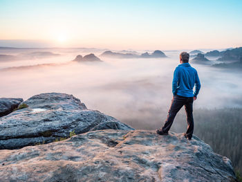 Lone man hiker relaxing on the mountain and watching sunset over the misty valley