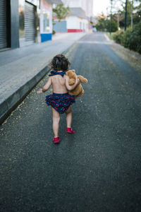 Playful baby girl with teddy bear running on road