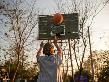 Rear view of senior man playing basketball at sunset