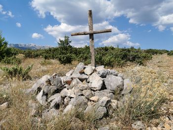 Cross on rock on field against sky