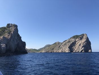 Rock formations by sea against clear blue sky