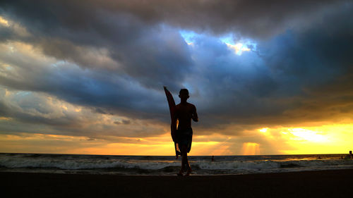 Silhouette man standing on beach against dramatic sky