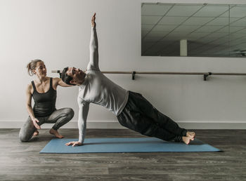 Female personal trainer coaches male client doing a sideways plank