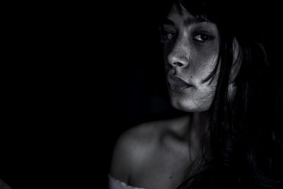 Close-up portrait of young woman smoking against black background