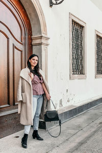 Full length portrait of woman standing against building