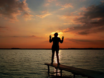 Silhouette man standing on sea against sky during sunset