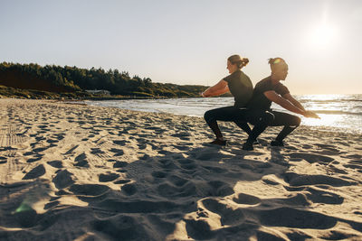 Man and woman practicing squats on sand at beach