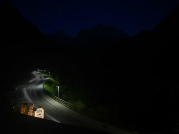 Illuminated road by mountains against sky at night