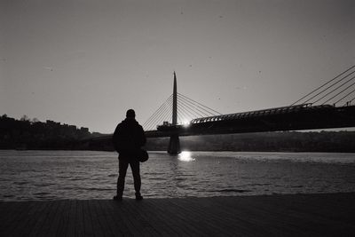 Rear view of silhouette man standing on suspension bridge against sky