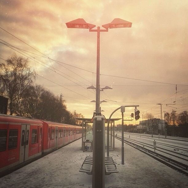 sky, architecture, built structure, street light, cloud - sky, power line, sunset, building exterior, railroad track, the way forward, electricity pylon, transportation, cable, railroad station, connection, rail transportation, cloudy, cloud, red, lighting equipment