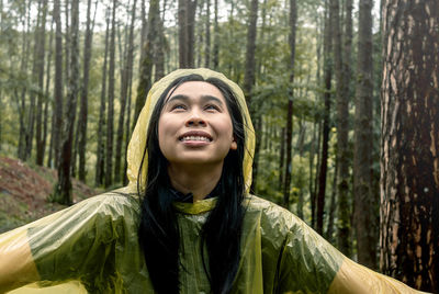 Woman wearing raincoat while enjoying rain in forest