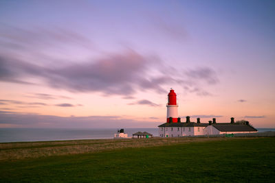 Lighthouse by sea against sky during sunset