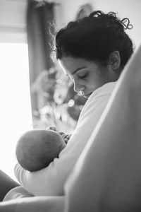 Close-up of mid adult woman breastfeeding newborn girl at home
