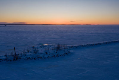 Scenic view of sea against snow covered land during sunset