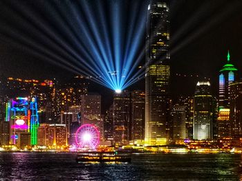 Illuminated buildings by sea against sky at night