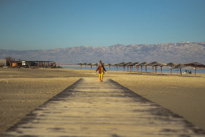 Mid distance view of girl walking on boardwalk at beach
