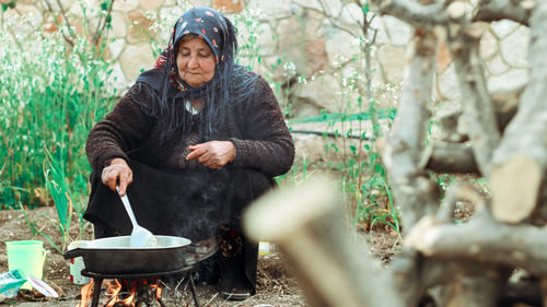 An elderly woman and her husband cook in the backyard of the house.