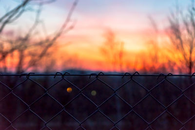 Close-up of chainlink fence against sky during sunset