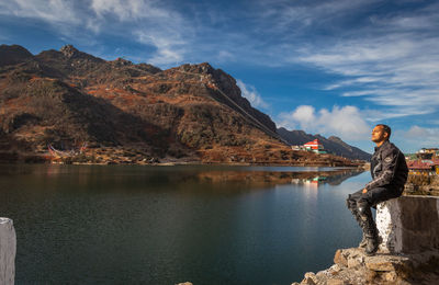 Man looking at lake by mountain against sky