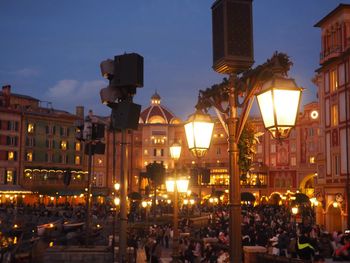 People on illuminated street amidst buildings in city at dusk