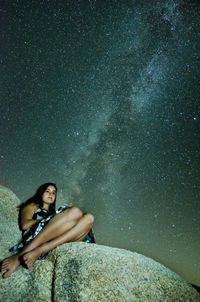 Teenage girl sitting on rock against star field