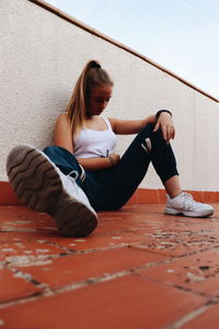 Full length of woman sitting on floor against wall