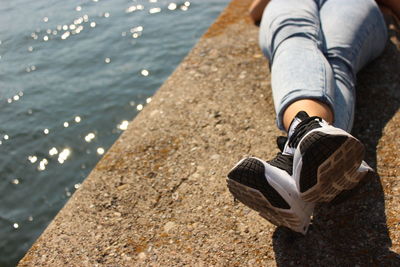 Low section of man wearing shoes relaxing on retaining wall by sea