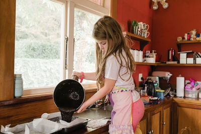 Girl standing on a chair pouring brownie mixture in a pan