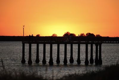 Silhouette pier over lake against orange sky