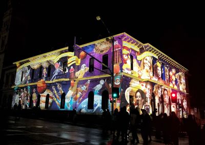 People walking on illuminated street amidst buildings at night