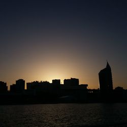 Silhouette buildings by river against sky during sunset