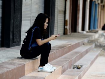 Side view of mid adult woman using smart phone while sitting on steps