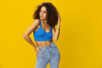 Young woman standing against yellow background