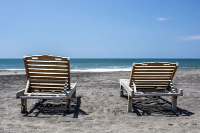 Deck chairs on beach against sky