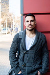 Front view of a fashionable young man standing against red wall