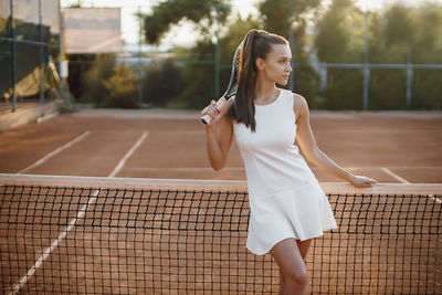 Smiling woman holding tennis racket at sorts court