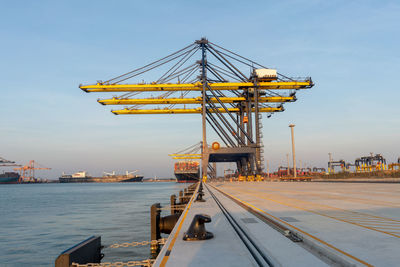 Cranes at harbor against sky