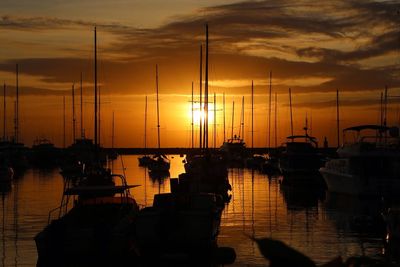 Silhouette sailboats moored on harbor against sky during sunset