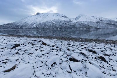 Frozen lake by snowcapped mountain against sky