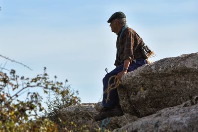 Mature man sitting of rock against sky