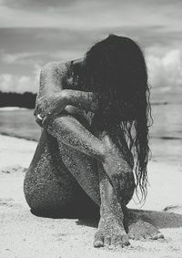 Naked messy woman sitting at beach