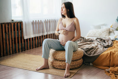 Tender young pregnant woman in underwear holding her belly sits in the interior of the bedroom 