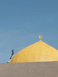 A man painting the yellow dome at mosque