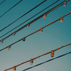 Low angle view of light bulbs and cables against clear blue sky during sunset