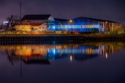 Illuminated industrial buildings with reflection on lake at night