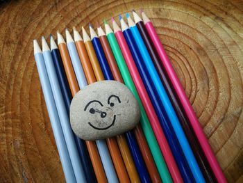 High angle view of stone with anthropomorphic face and colored pencils on wooden table