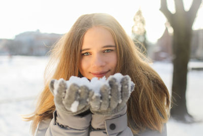 Portrait of smiling young woman holding snow in winter