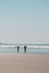 Silhouette couple walking on beach with surfboard