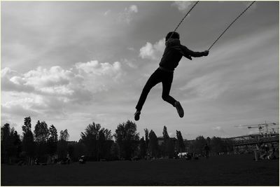 Rear view of man swinging in park against sky